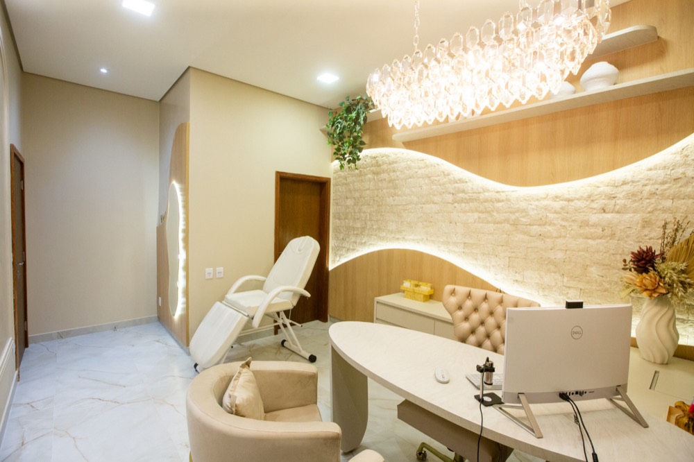 Consultório da Dra. Ana Flávia com mesa, poltronas, lustre de cristal e parede de pedra iluminada